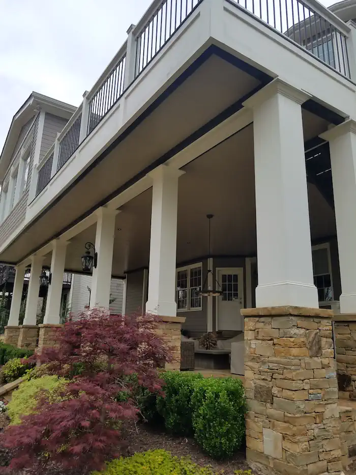 Two-story home with stone columns, covered porch, and landscaping